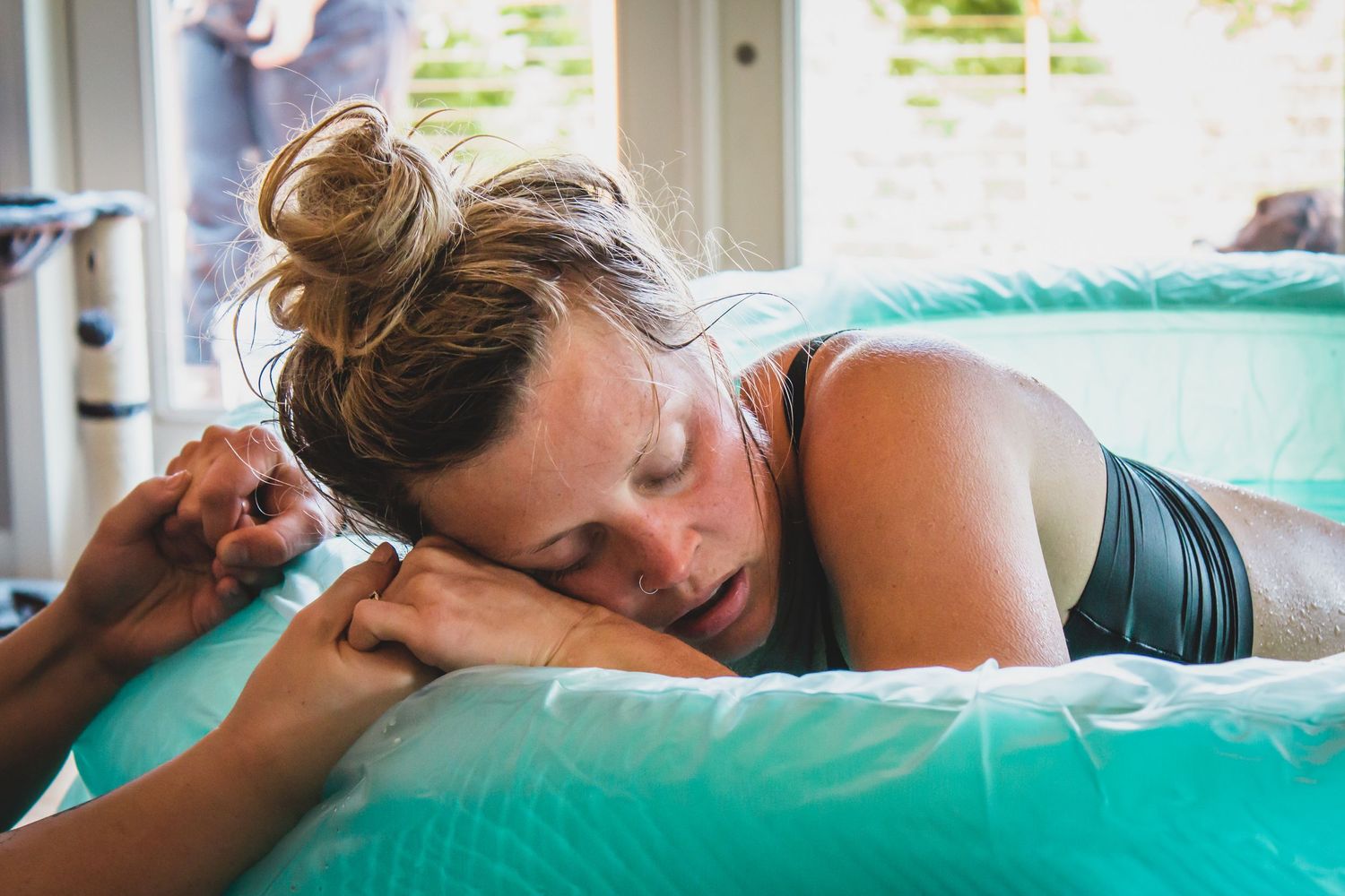 Home birth mother in pool holding birth doulas hands | Heart & Hands Birth Services | doula & photography