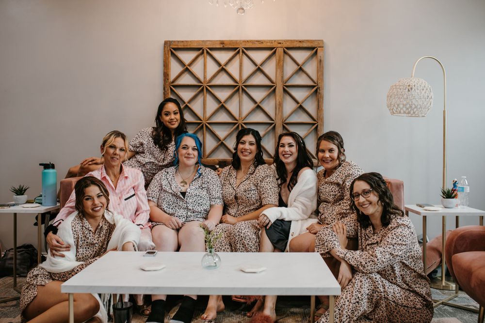 Group of nine bridesmaids in leopard print robes pose together smiling in bright modern bridal suite.