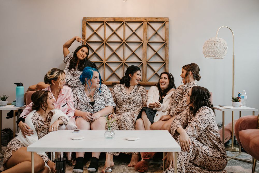 Bridesmaids in matching leopard print robes laugh together on pink velvet sofa during wedding morning preparations.