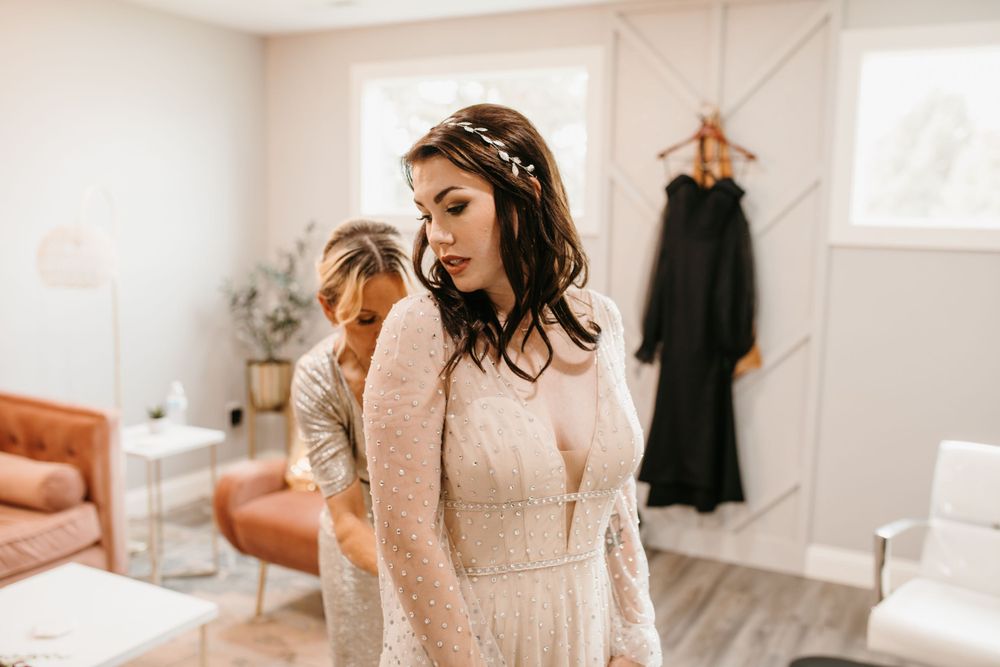 Bride in long-sleeve beaded wedding gown with floral headpiece gazes down in elegant bridal suite.