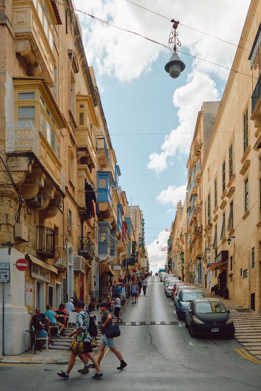 Steep uphill street in Valletta with traditional Maltese architecture and hanging balconies.