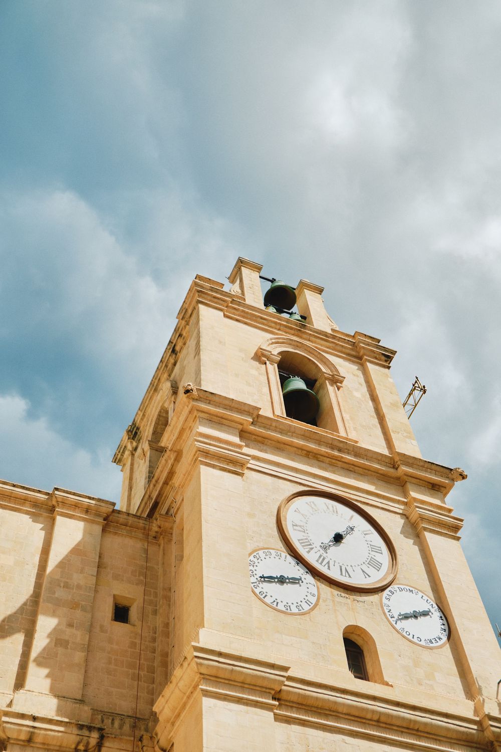 Historic church bell tower with multiple clock faces against cloudy blue sky.