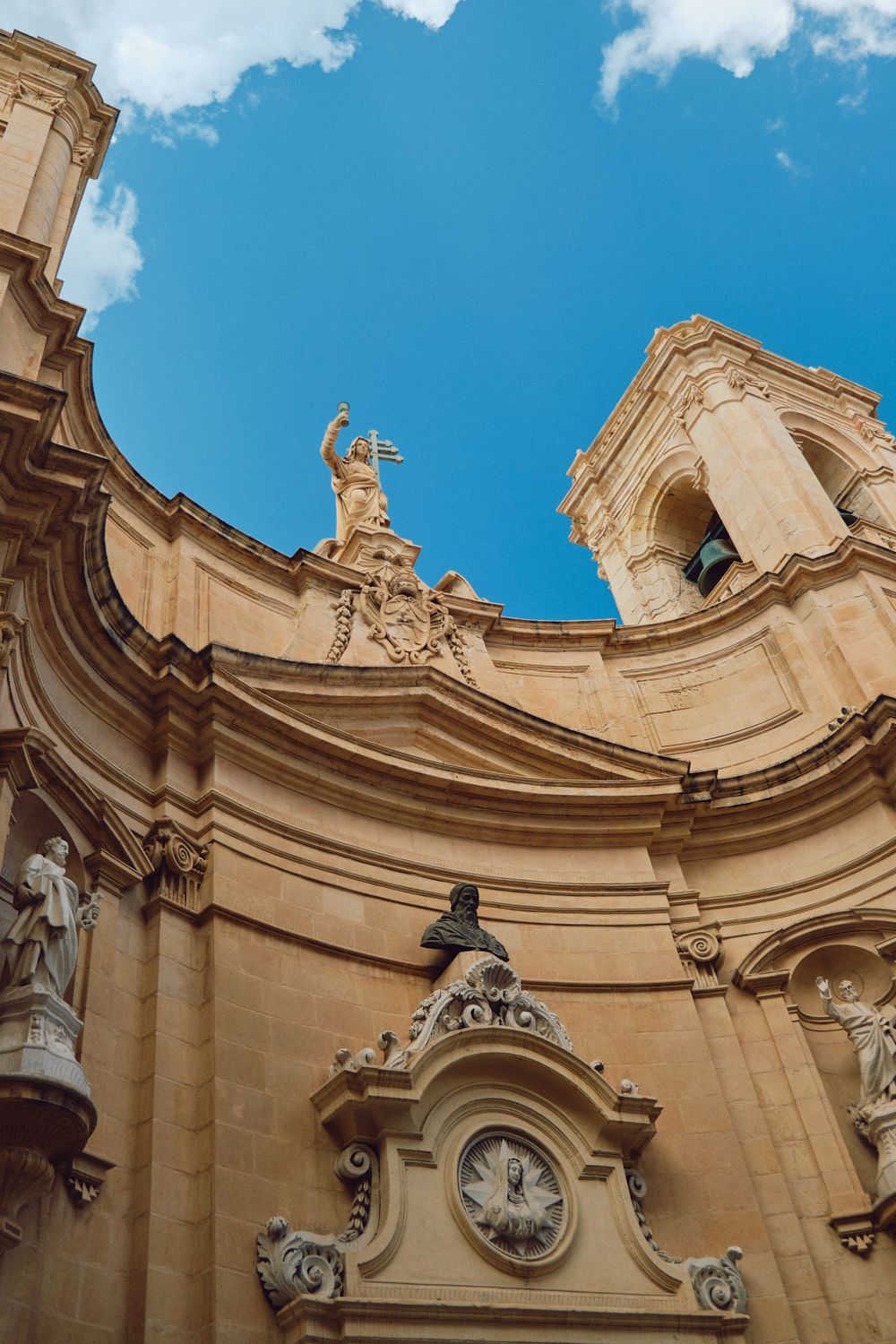 Ornate baroque church facade with statue and clock detail against bright blue sky.
