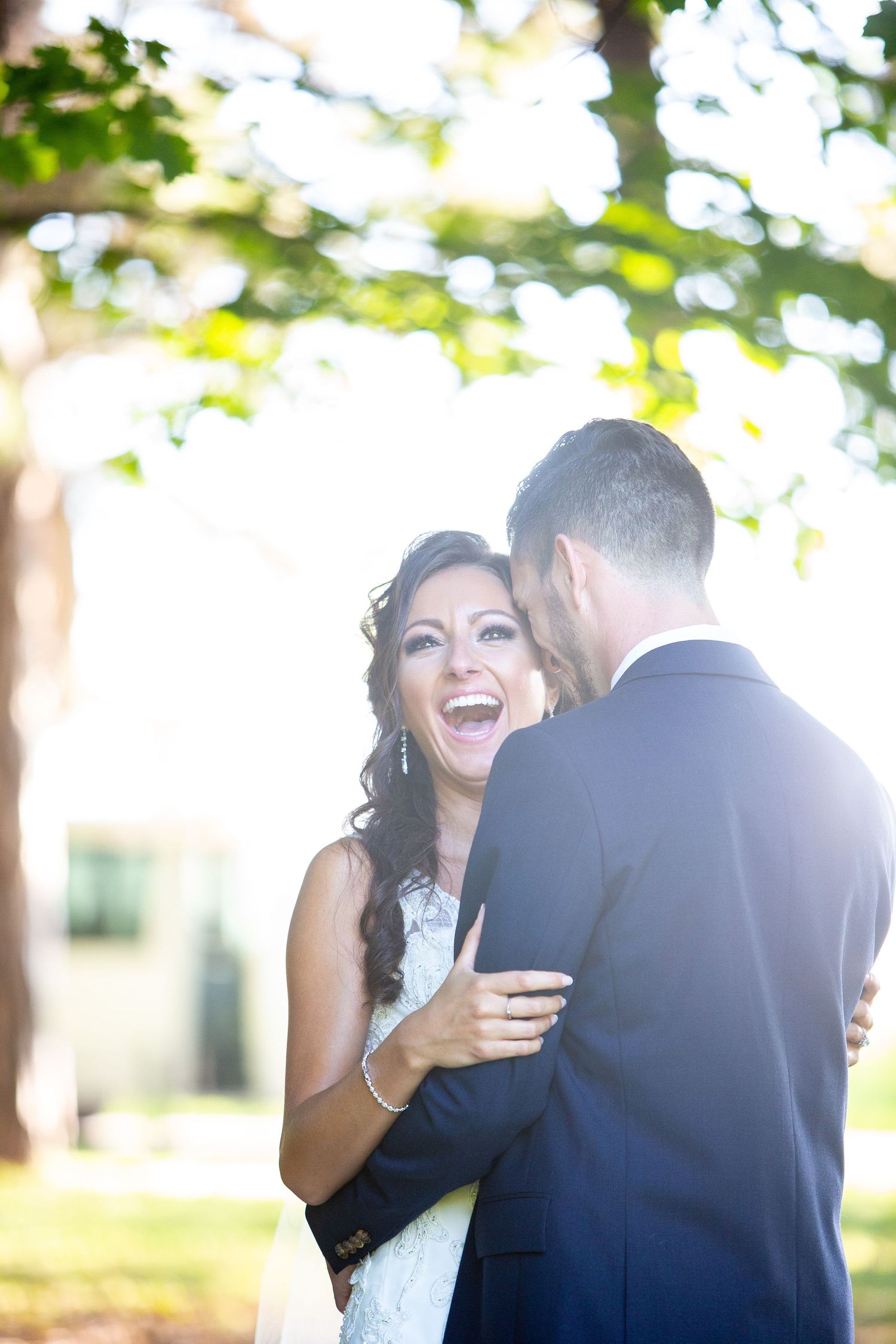 Joyful wedding moment captured outdoors with natural sunlight filtering through trees.