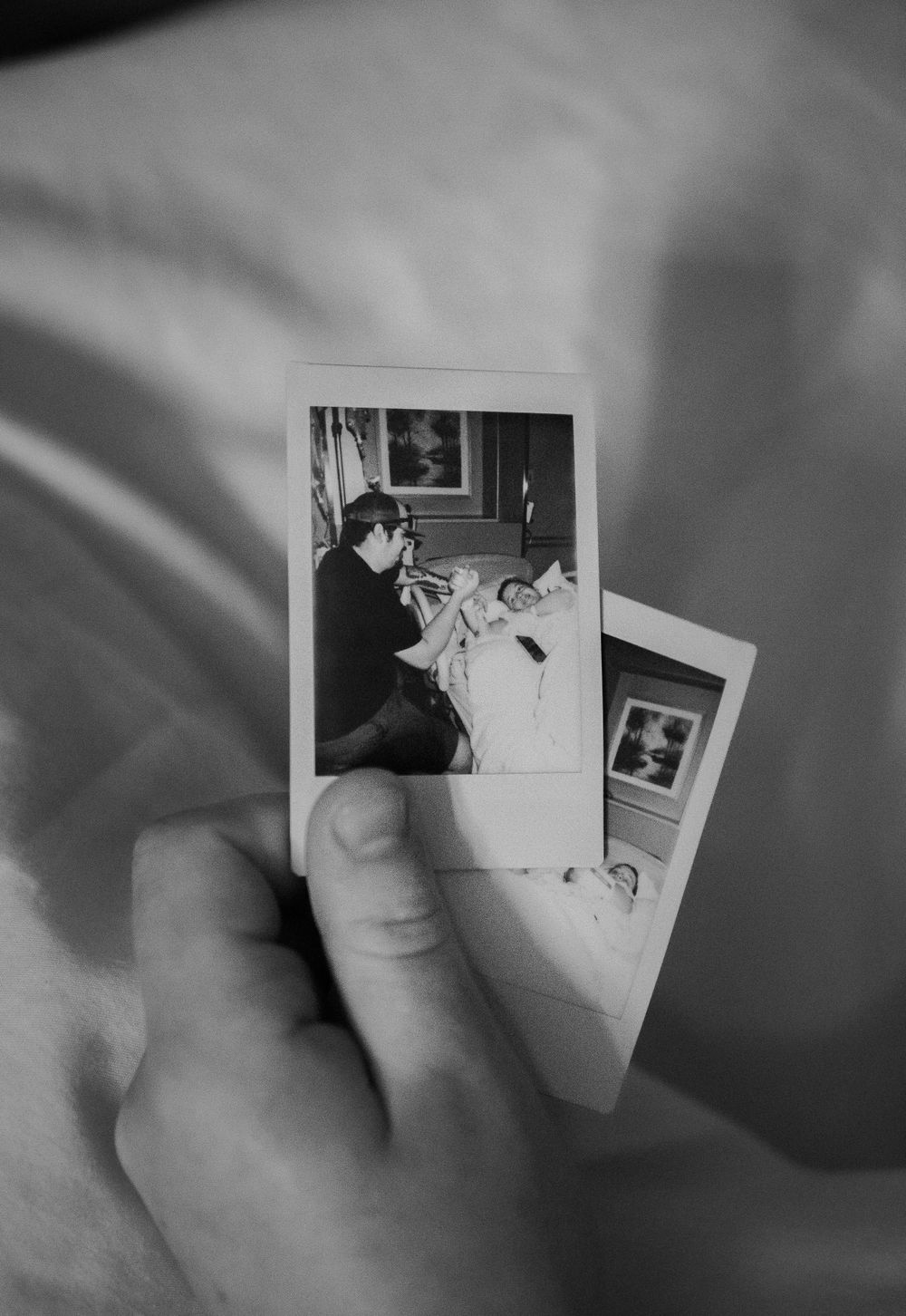 Hand holding vintage black and white photographs showing intimate family moments.