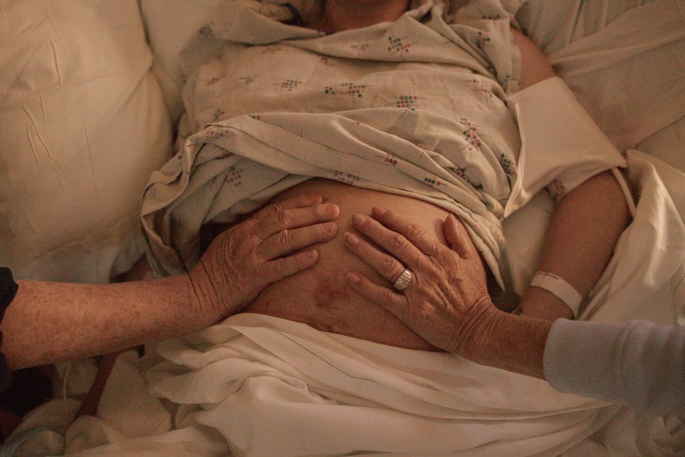 Hands rest gently on a patient's abdomen in a medical setting.