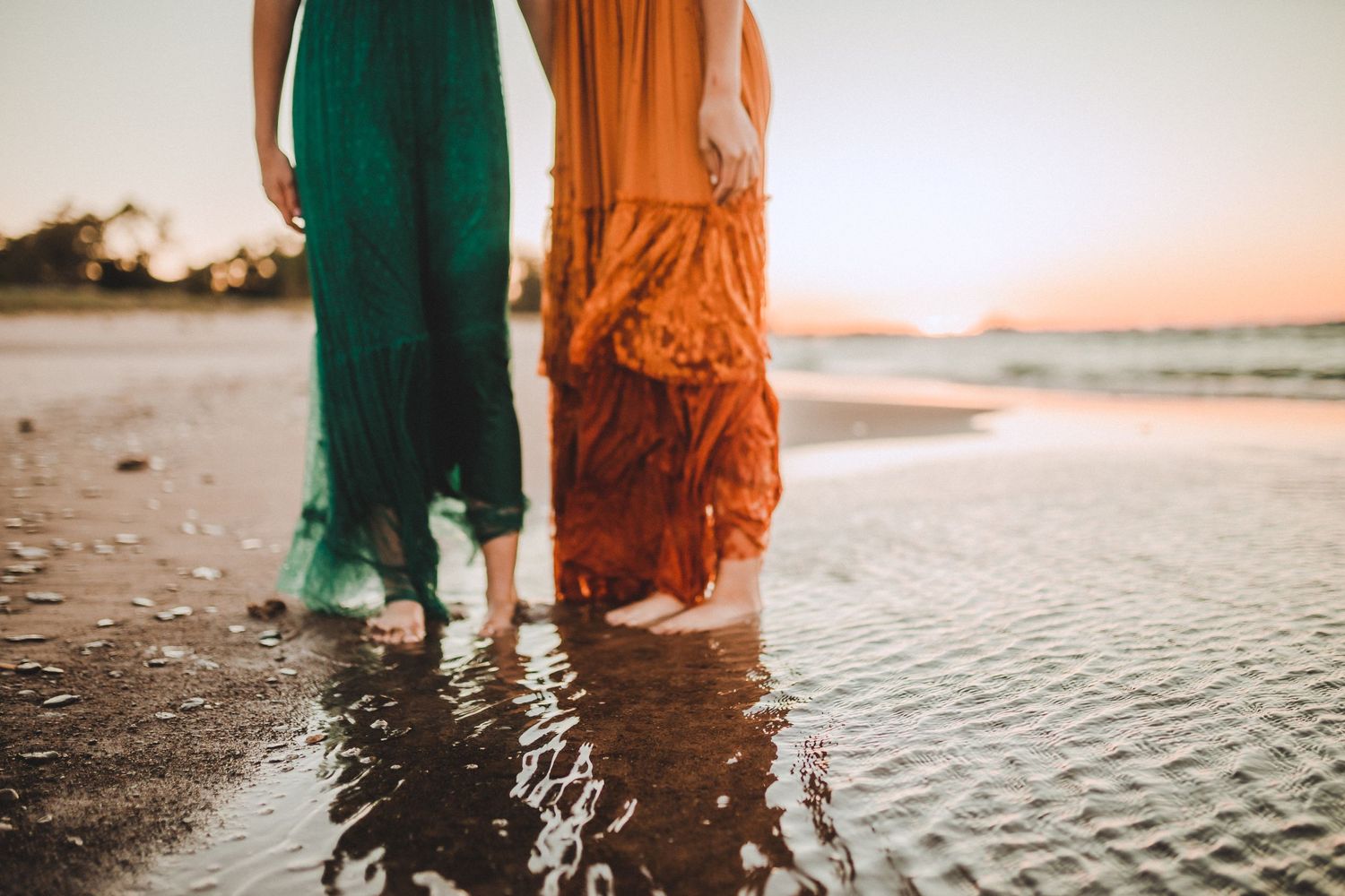 Close-up of two women wearing green and orange dresses standing in shallow ocean water.