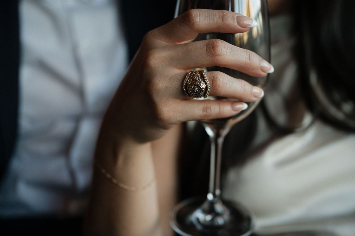 Hand holding wine glass showing detailed view of statement ring in soft lighting.