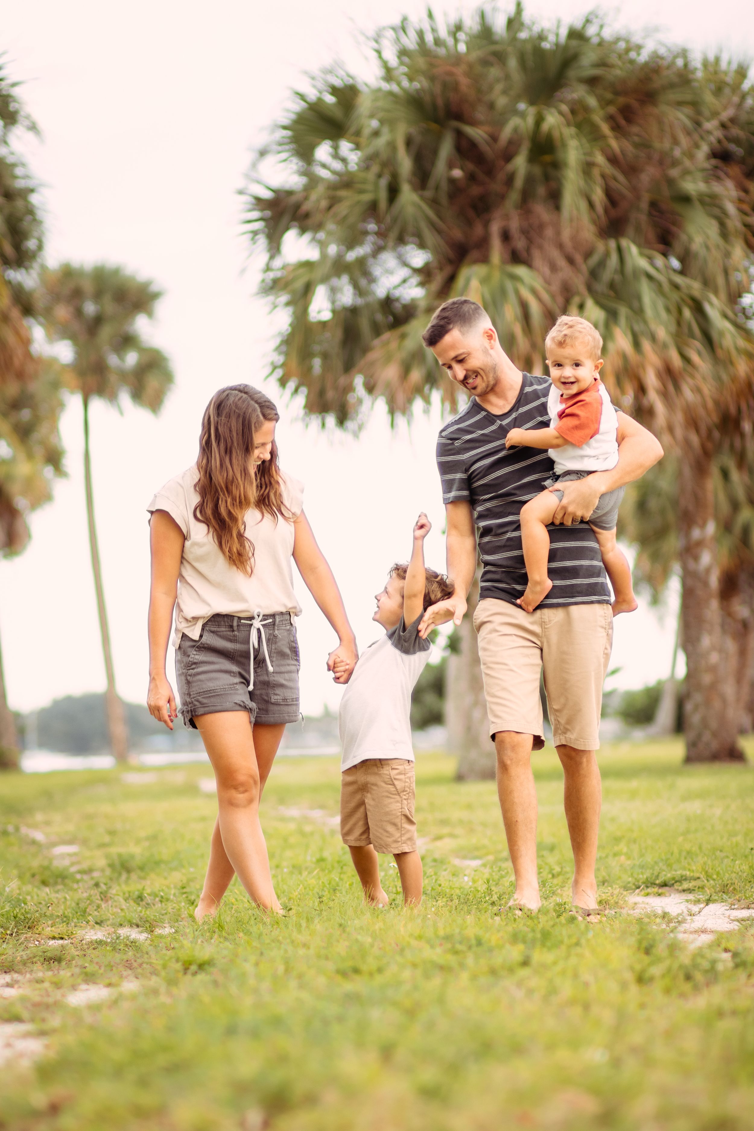Happy family with two young children playing outdoors in a tropical park with palm trees on a sunny day.