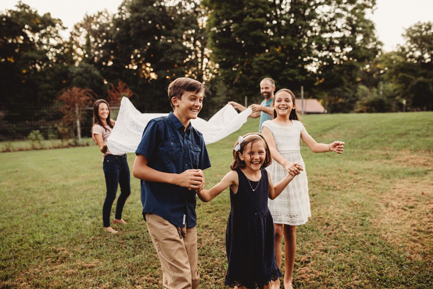 Kids laughing while running under a blanket that parents are holding