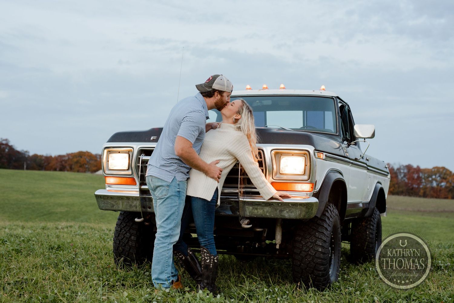 Couple posing against a lifted Ford pickup truck in a scenic rural field.