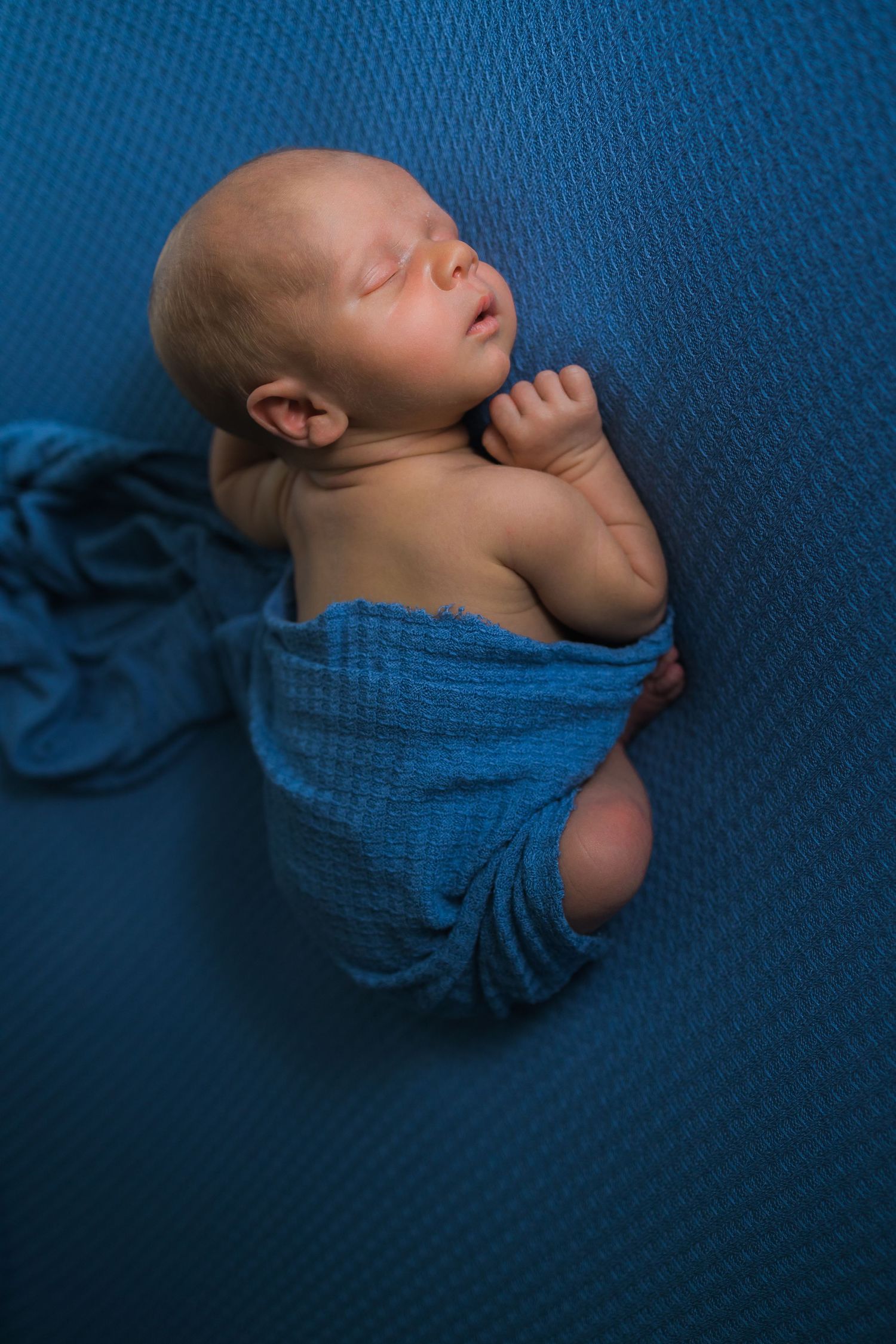 Newborn baby sleeping wrapped in blue textured blanket.