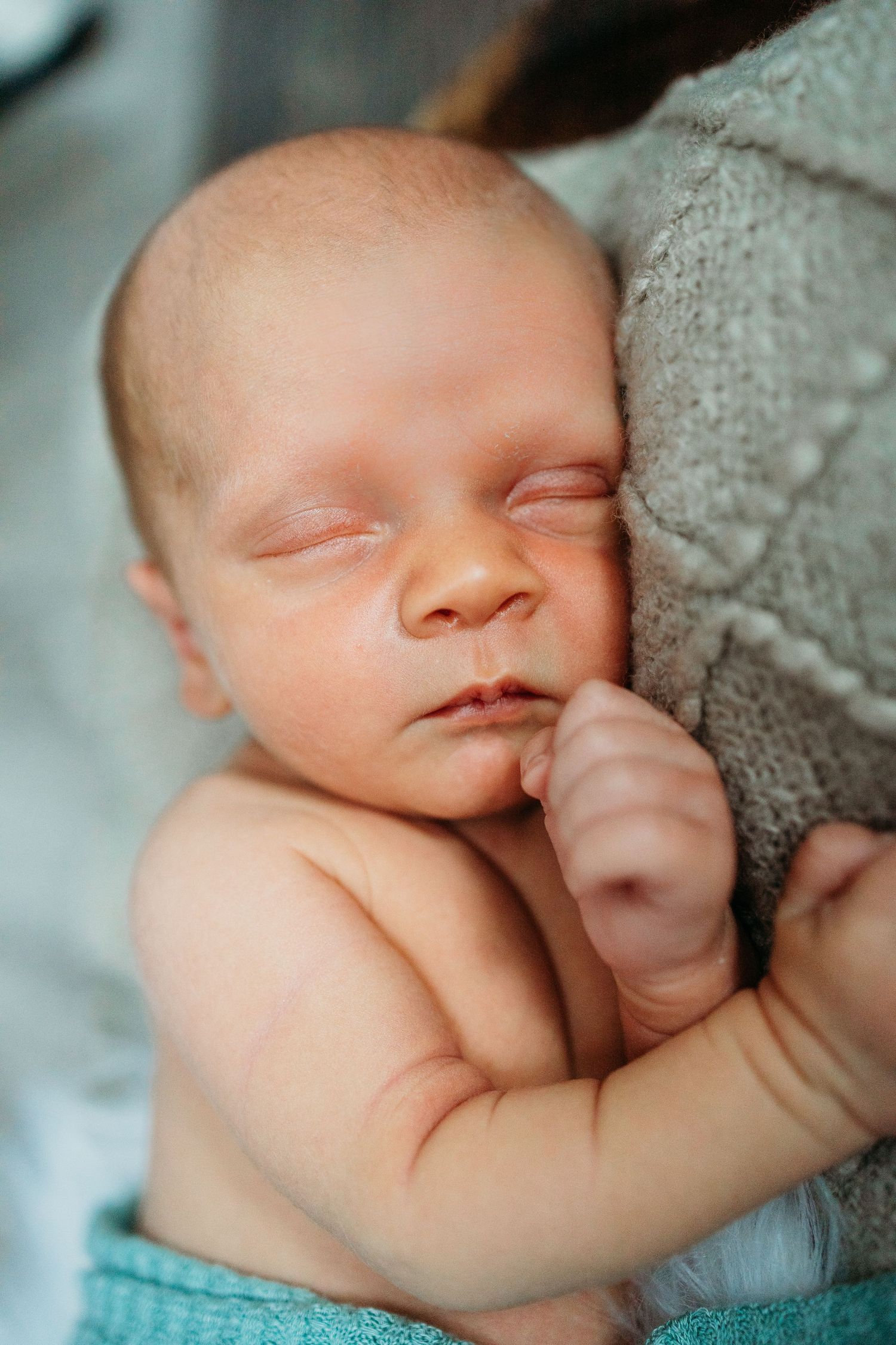 Sleeping newborn rests peacefully against a gray blanket in soft lighting.