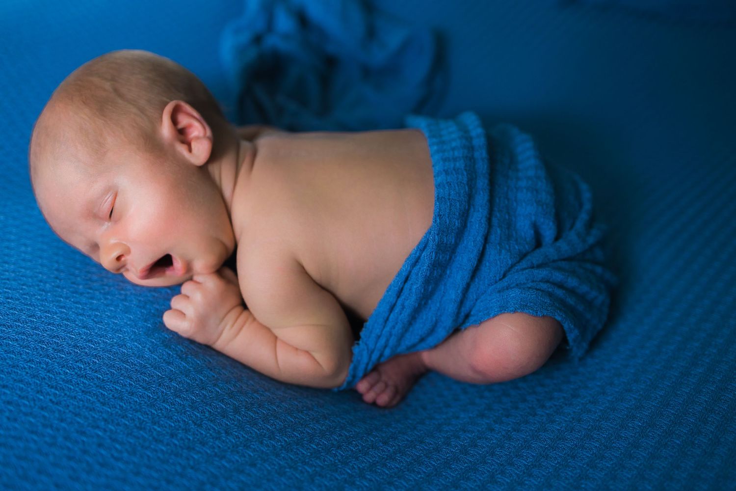 Peaceful newborn sleeping on bright blue textured surface.