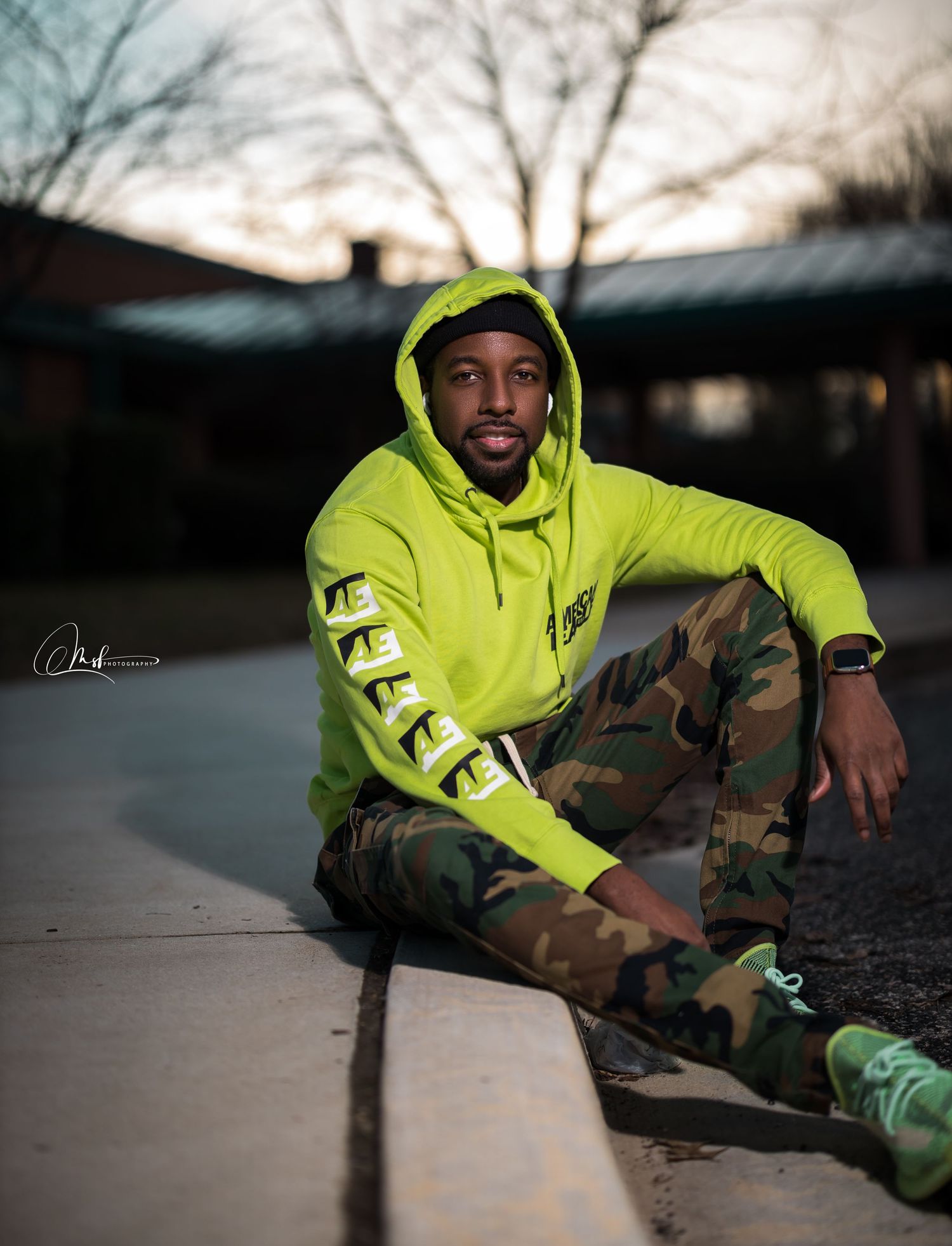Streetwear fashion shoot with model in bright yellow hoodie and camo pants at dusk.