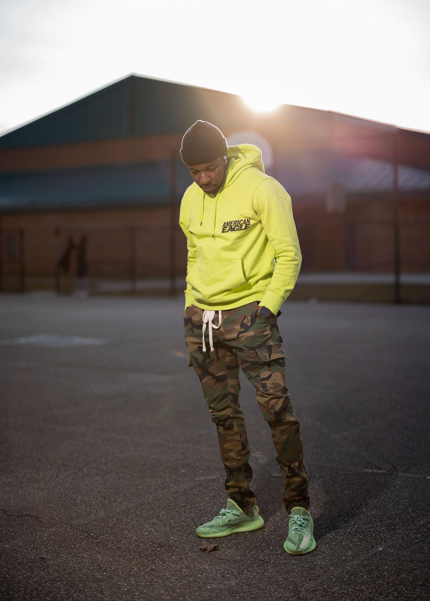 Street style photo of model in yellow hoodie and camo cargo pants with matching green shoes.