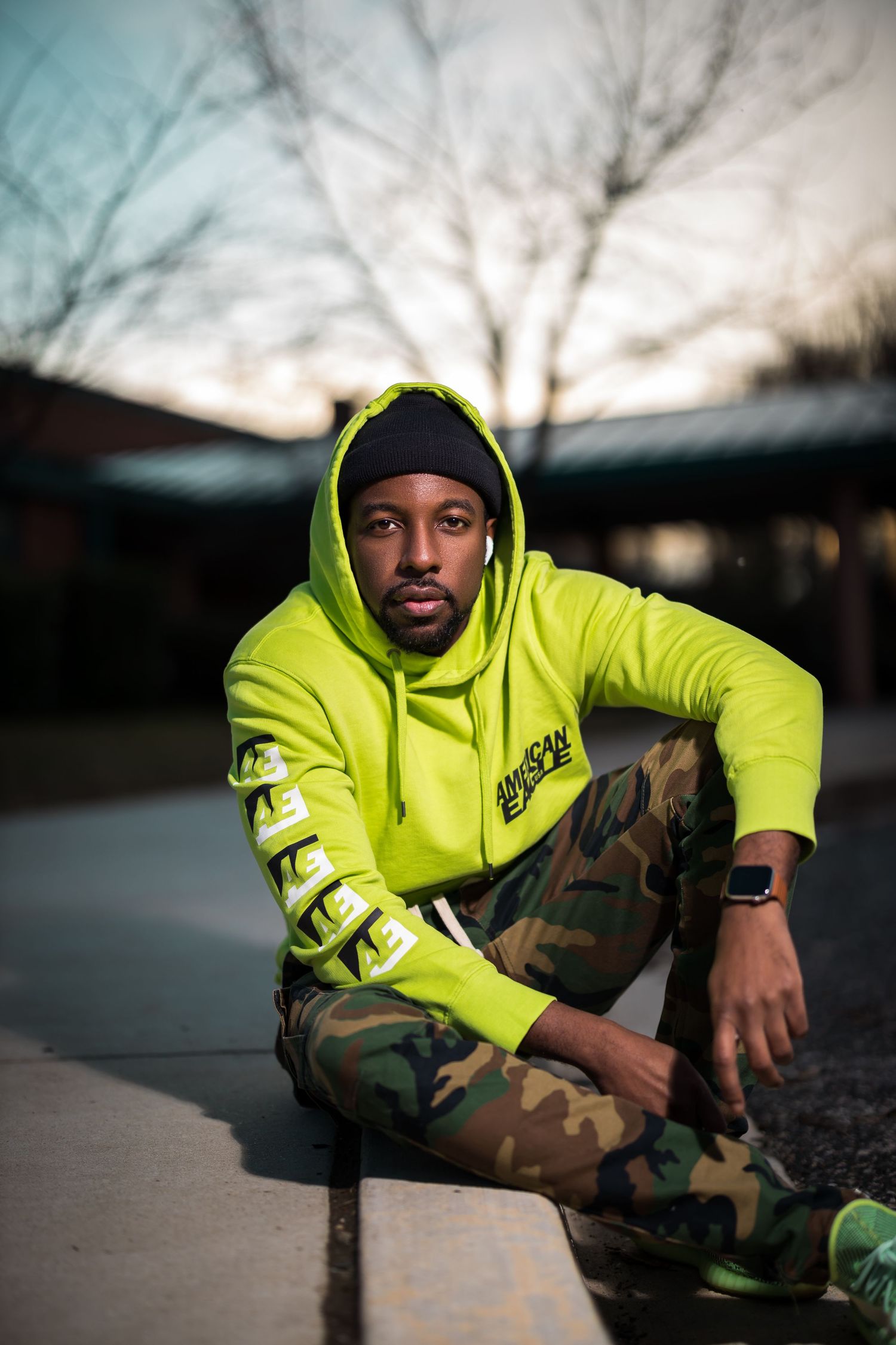 Urban fashion portrait featuring neon hoodie and camouflage pants in sunset lighting.