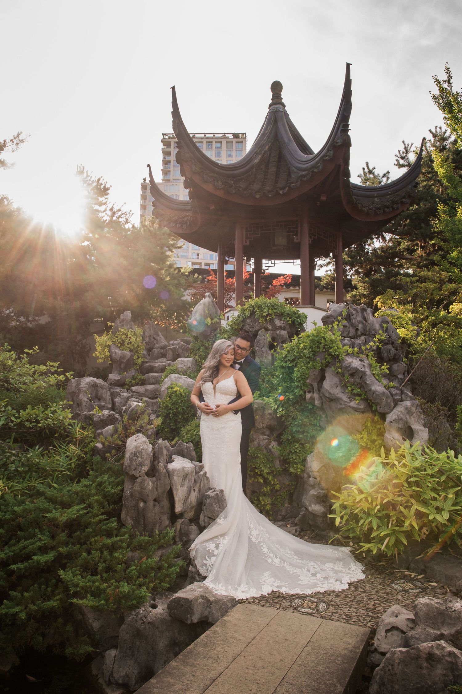 A bride in a mermaid gown poses beneath a Chinese pagoda with sunlight streaming through.