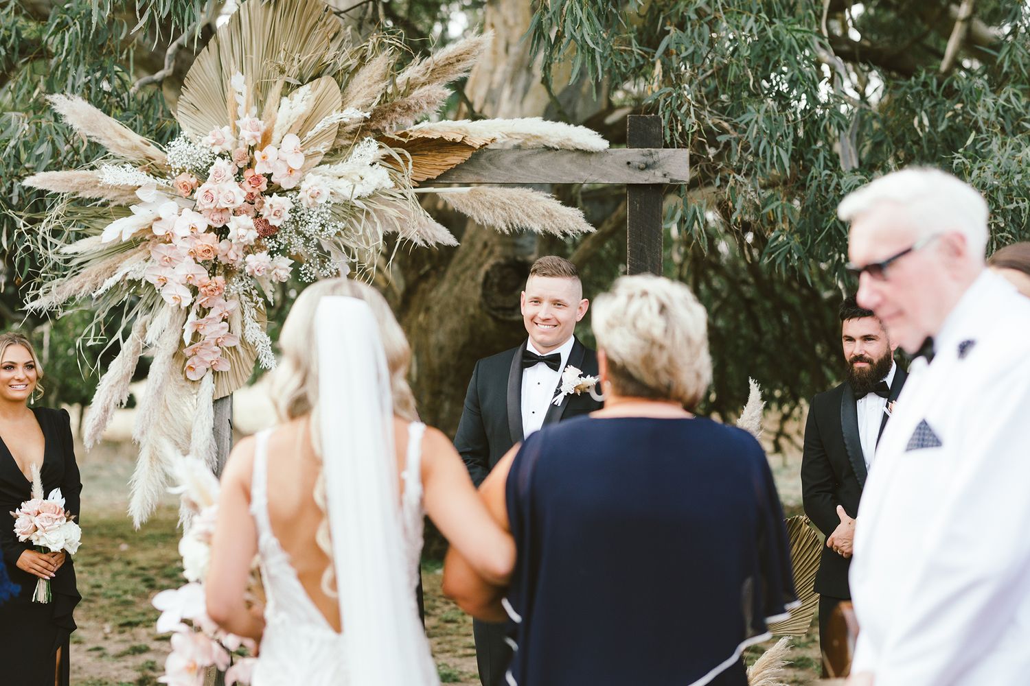 Wedding ceremony under natural arch with dried palm arrangements and eucalyptus trees in background.