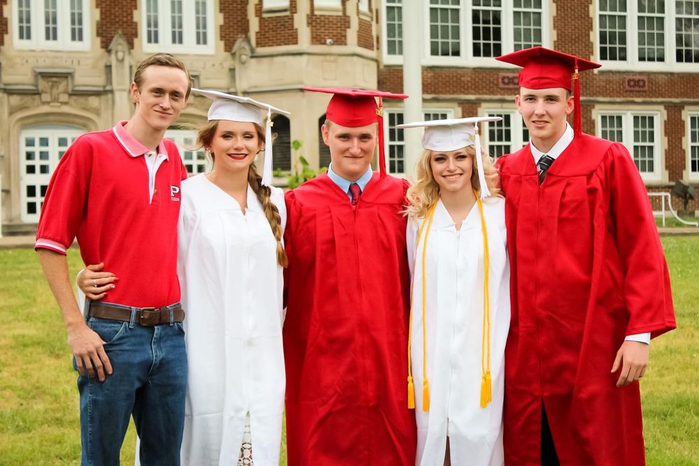 A group of graduates in red and white robes lined up next to a brick building during commencement.