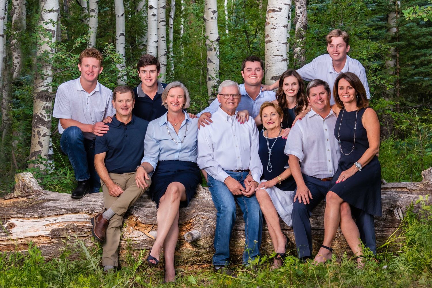 Three generations of a family sitting on a log in the woods with aspens