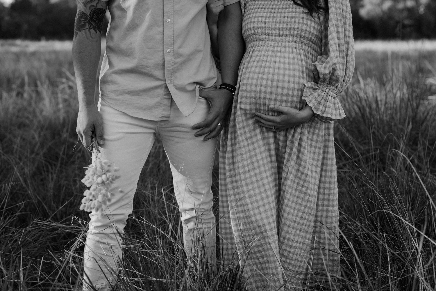 Black and white maternity photo showing couple in gingham dress and white pants.