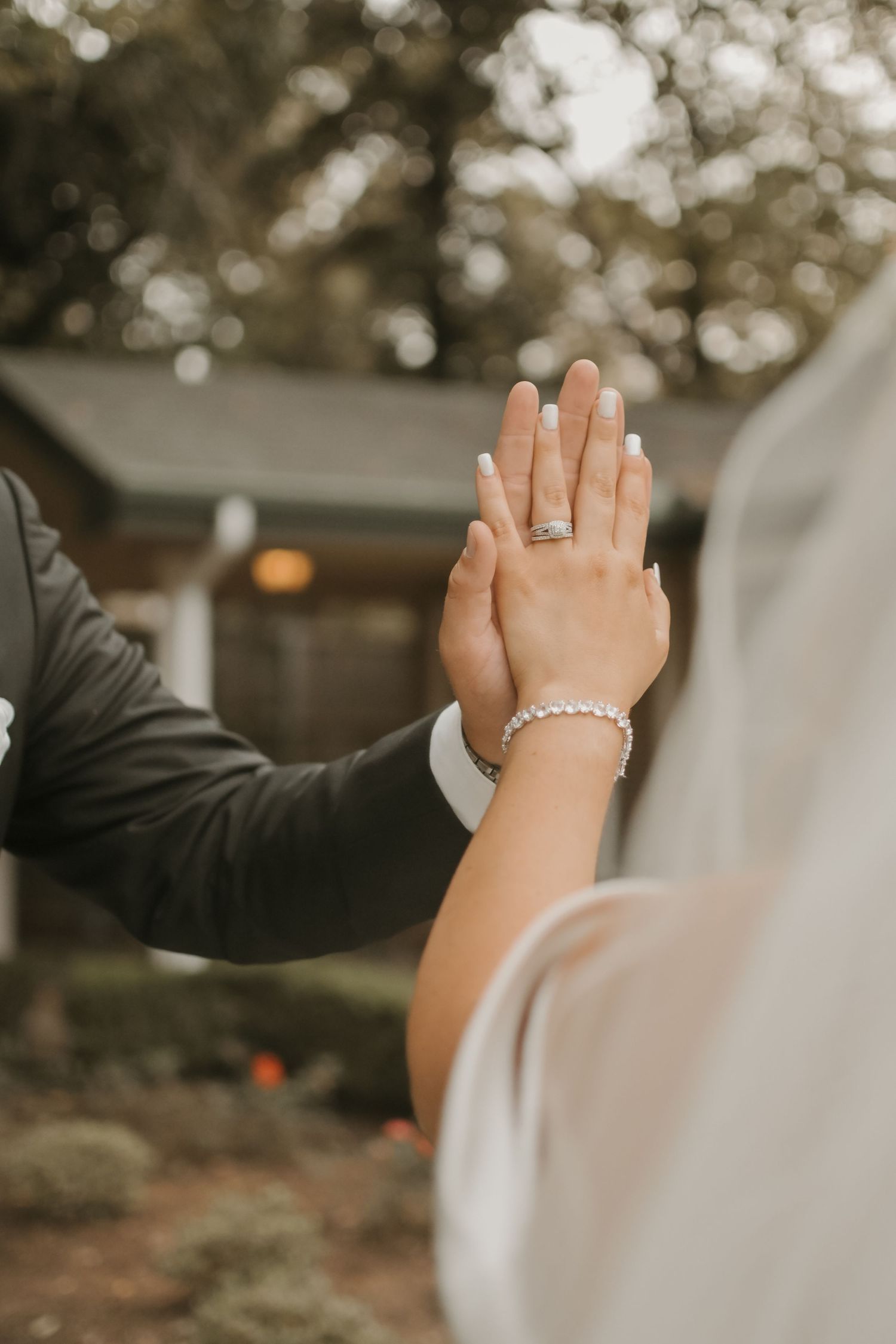 Wedding ceremony hands raised showing rings and bracelets against natural outdoor backdrop.