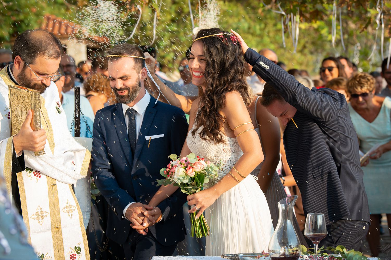 couple smiling during the isaias dance at their outdoor wedding ceremony while guests throw rice