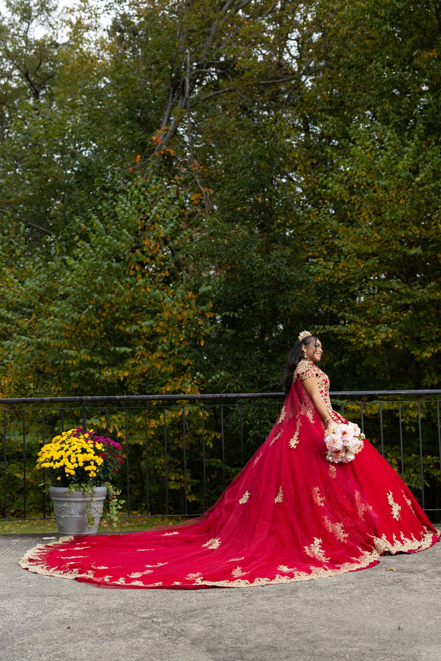 Dramatic red ball gown with gold appliques and long train photographed in autumn setting.
