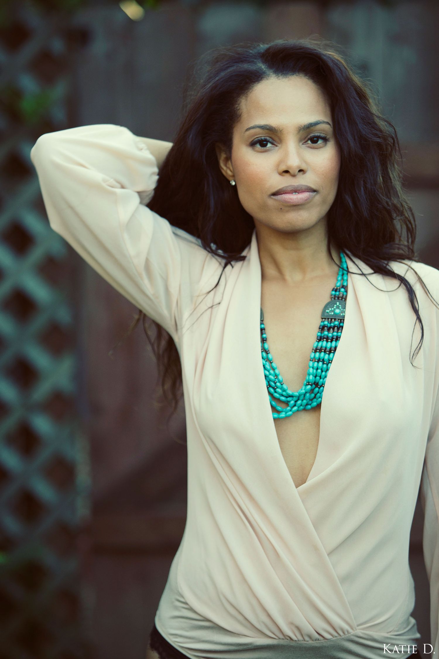 Woman in a cream wrap blouse wearing a turquoise beaded necklace posing outdoors.