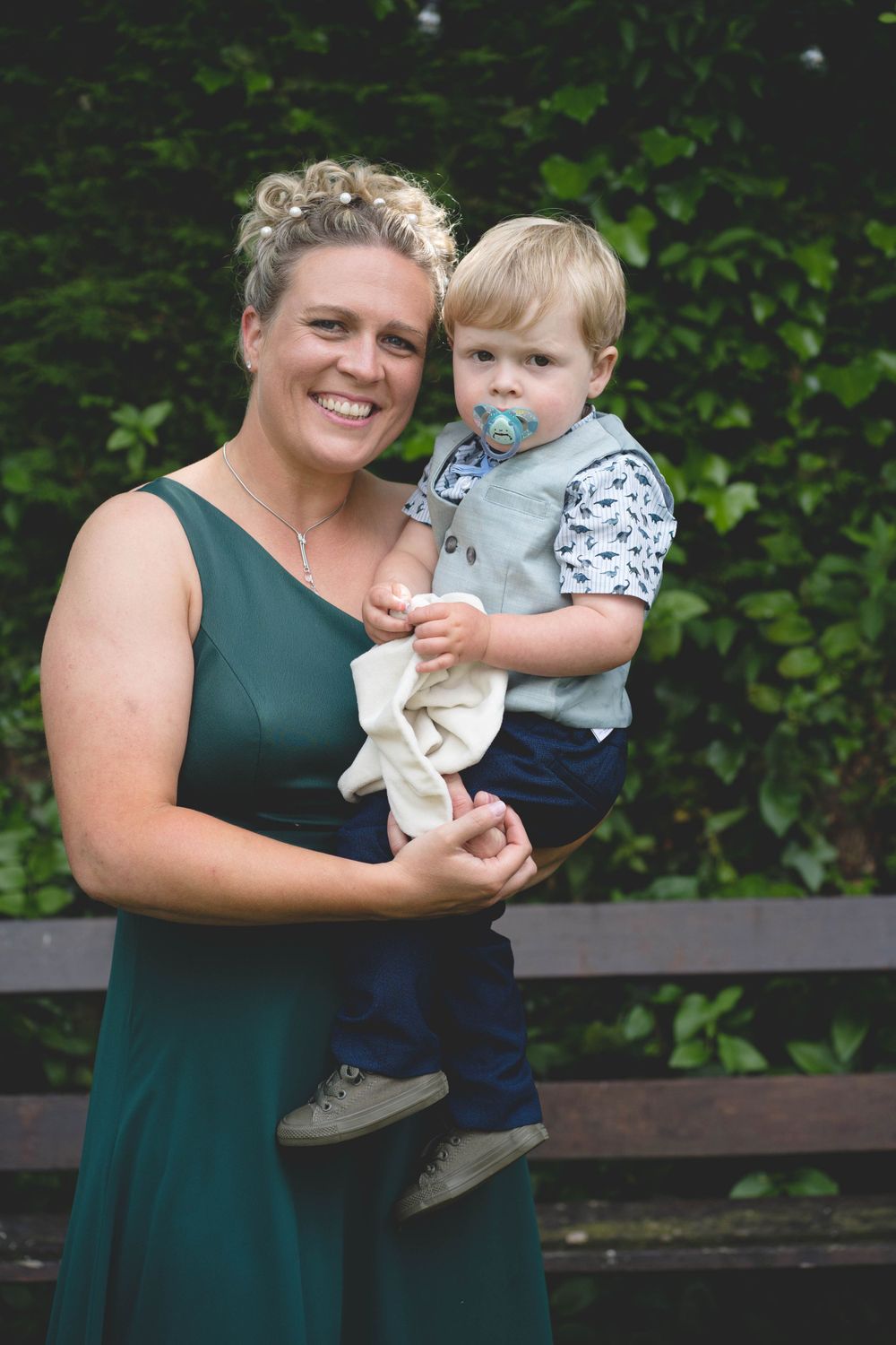 Parent and toddler in formal attire posing together against green foliage.