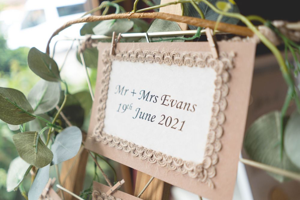 Elegant wedding signage with decorative lace borders displayed against greenery backdrop.