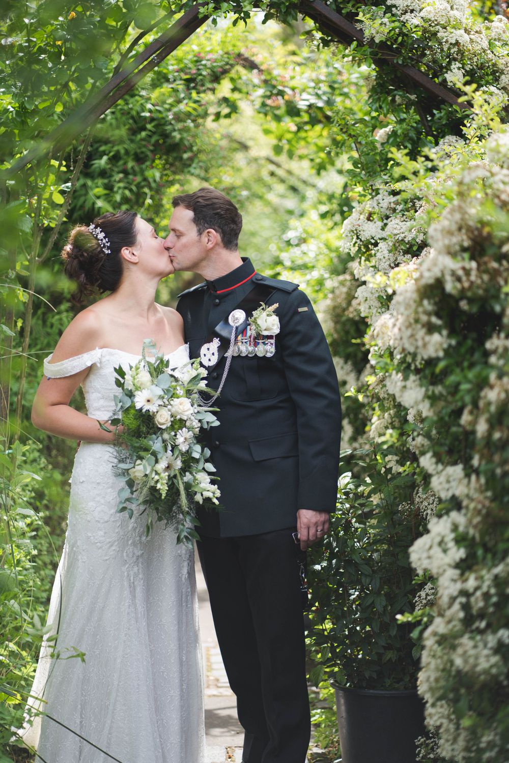 Newlyweds sharing intimate kiss in garden setting with white floral backdrop.