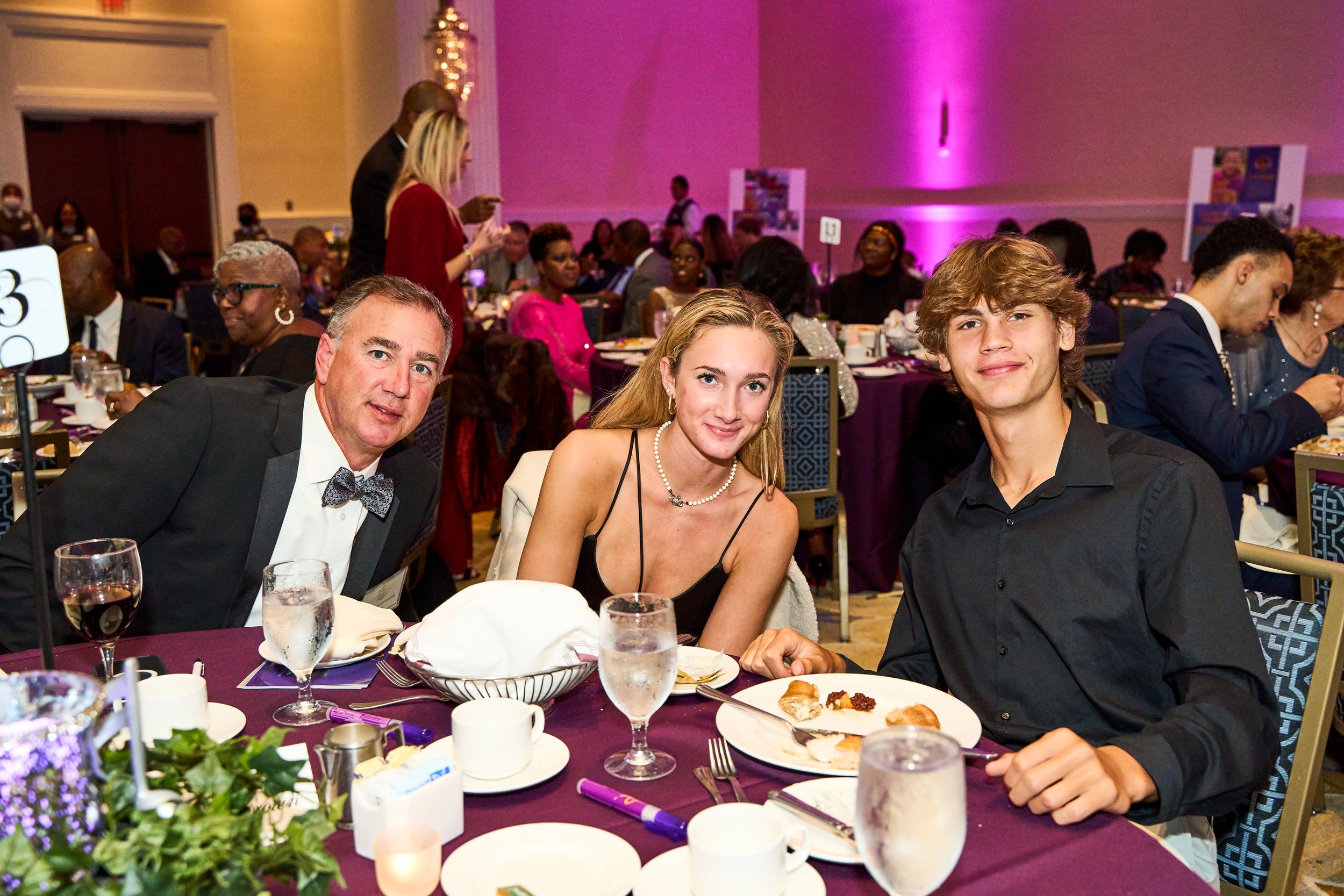 Three guests seated at an elegantly decorated table with purple accents at a formal dinner event.
