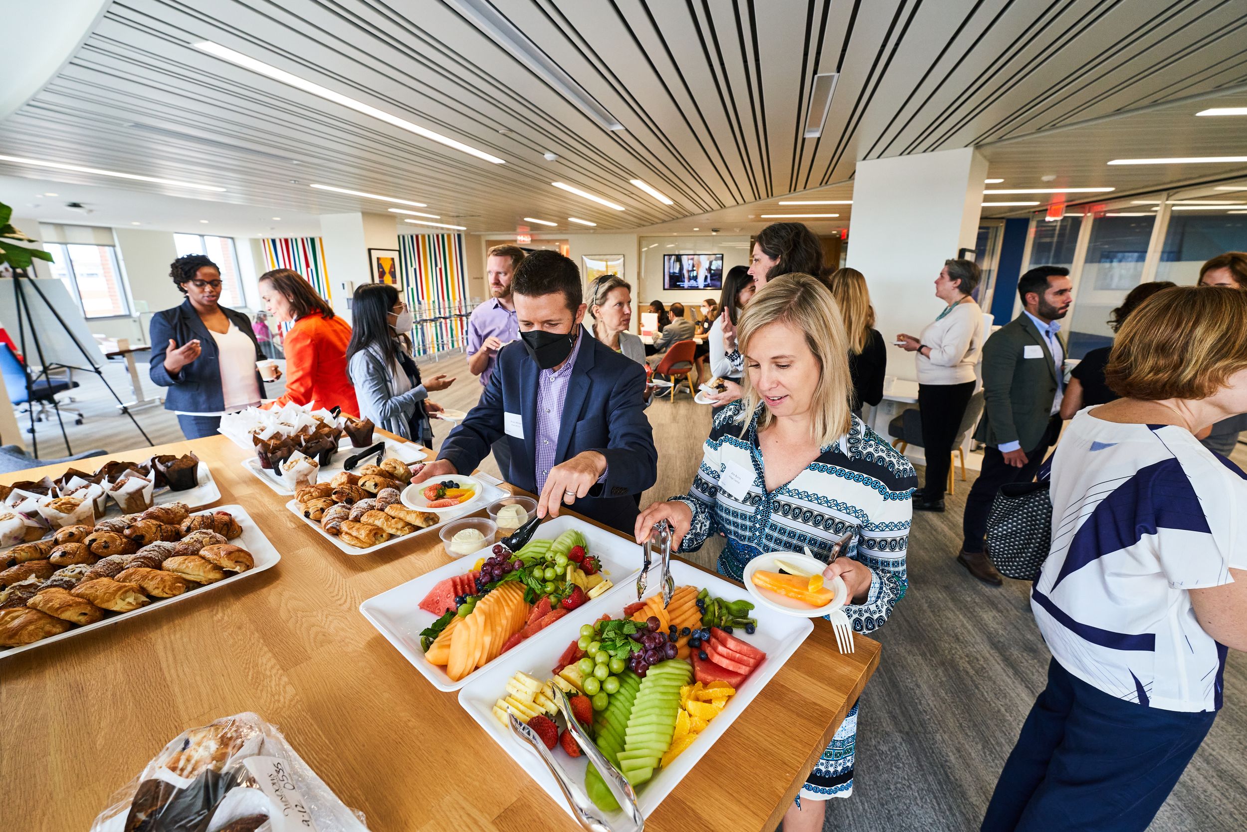 People serving themselves at buffet line with modern interior design and wood ceiling.
