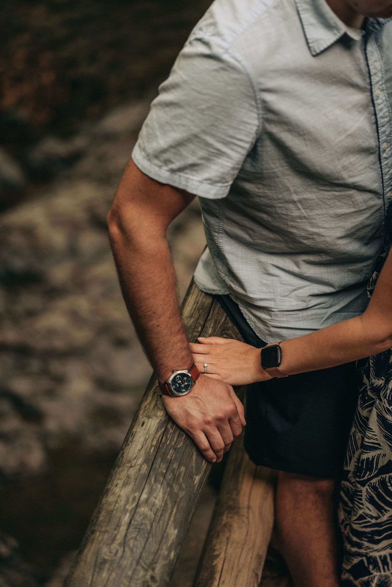 Person in a light blue shirt leaning against wooden railing wearing a smart watch.
