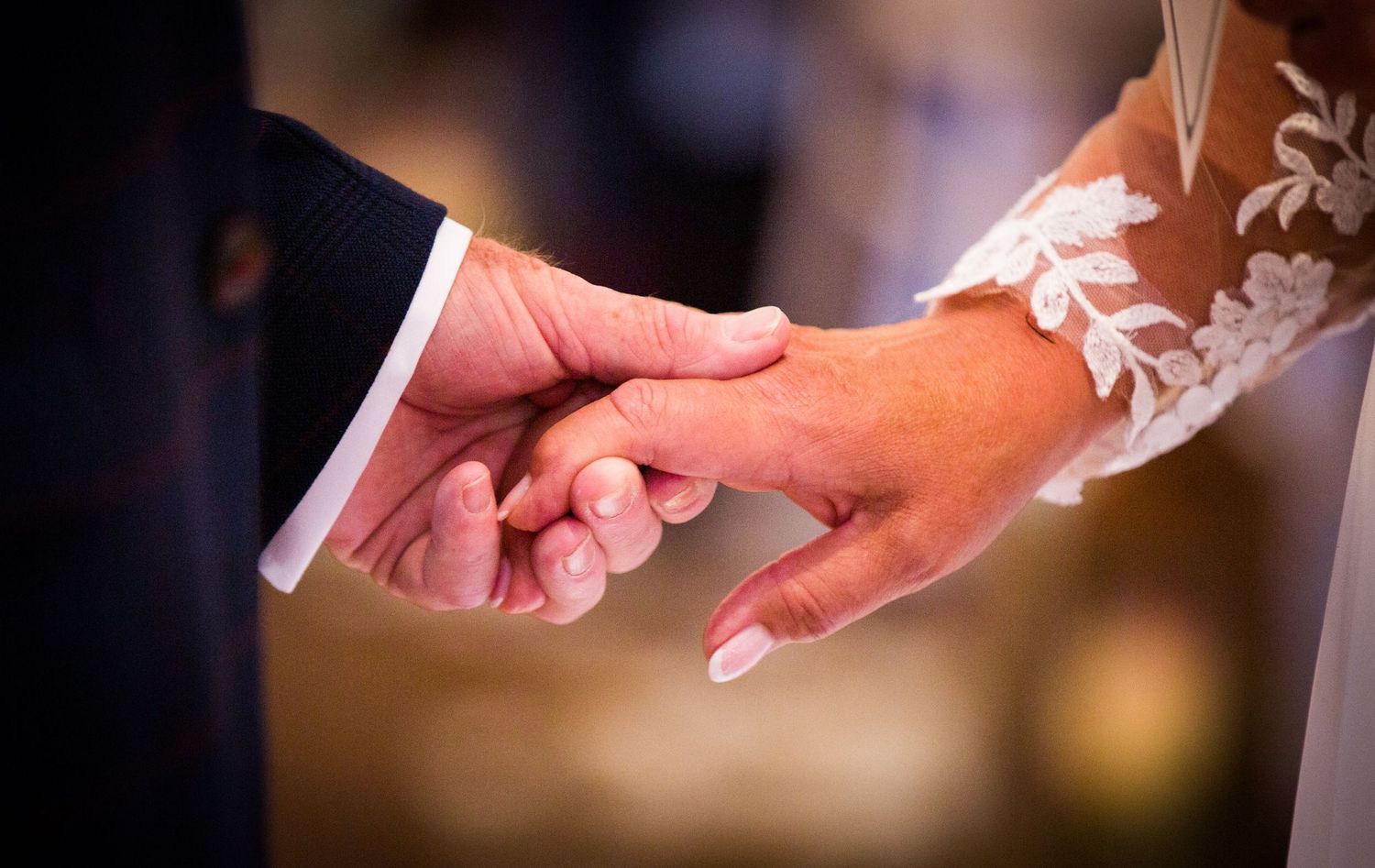 Close-up details of hands exchanging rings during wedding ceremony.