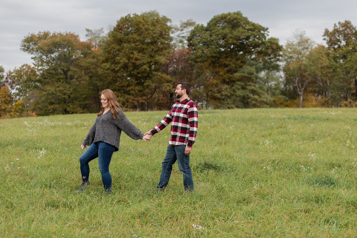 A couple enjoys a playful moment together on green grass during an autumn day.