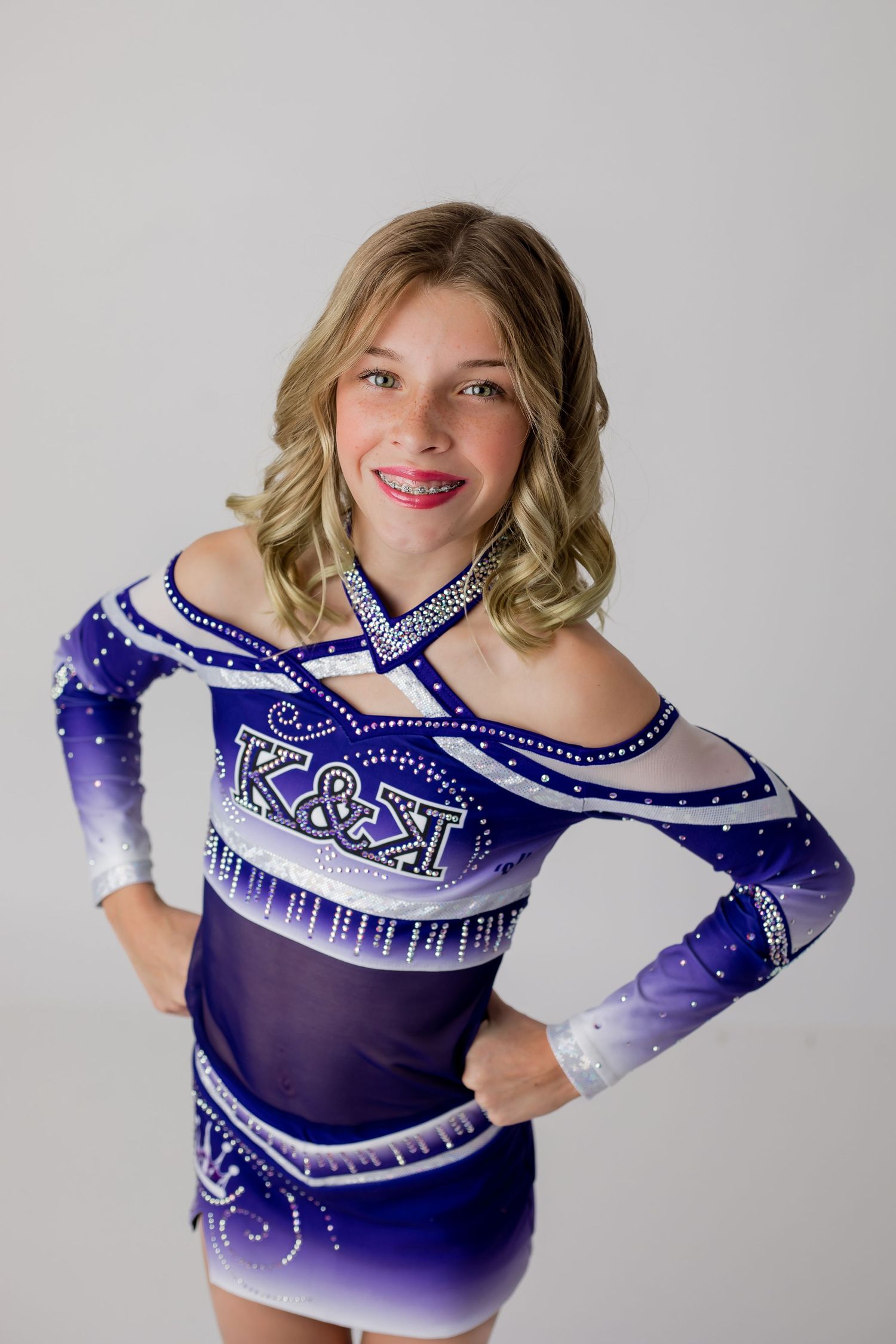 Cheerleader girl in her cheer uniform smiles and poses in front of a white backdrop for her cheer headshot portrait.