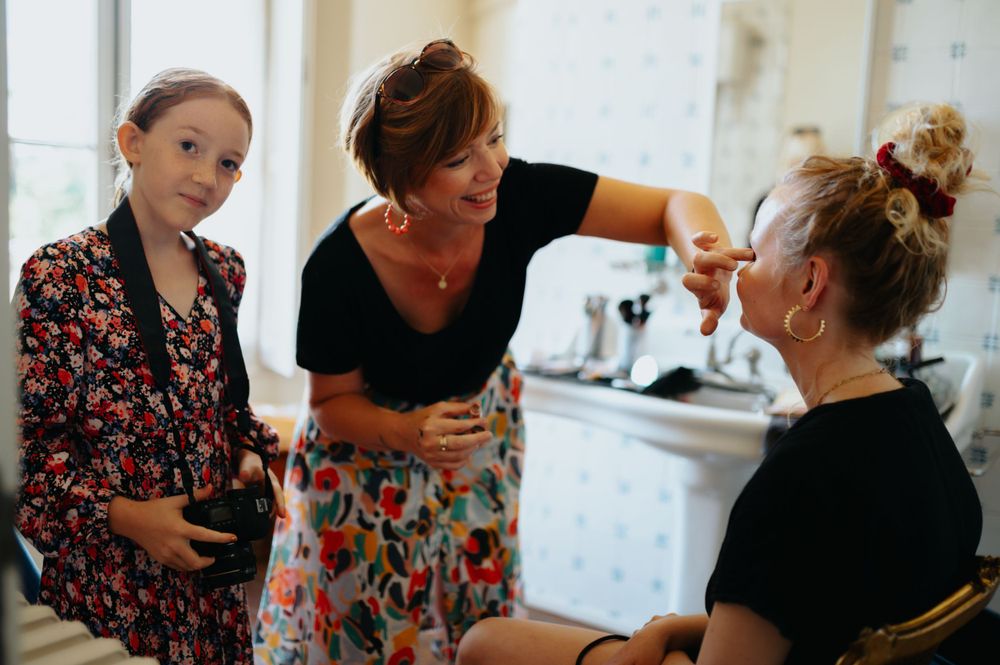 Three people gather in conversation during wedding preparations in a bright room.