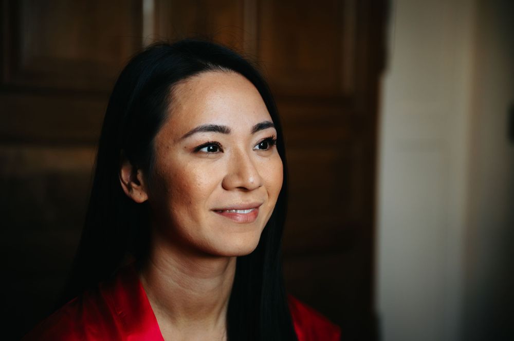 A woman in a red top smiles warmly in a moody indoor portrait.