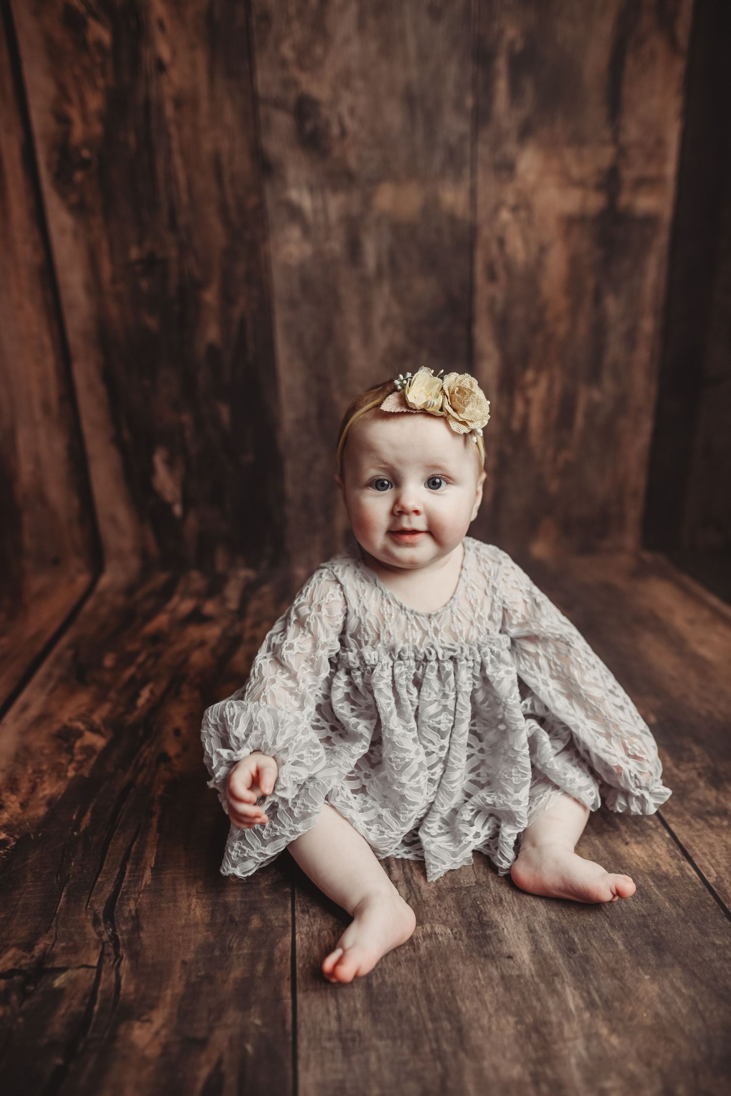 Vintage-style lace dress on wooden floor with dark brown backdrop for portrait photography.