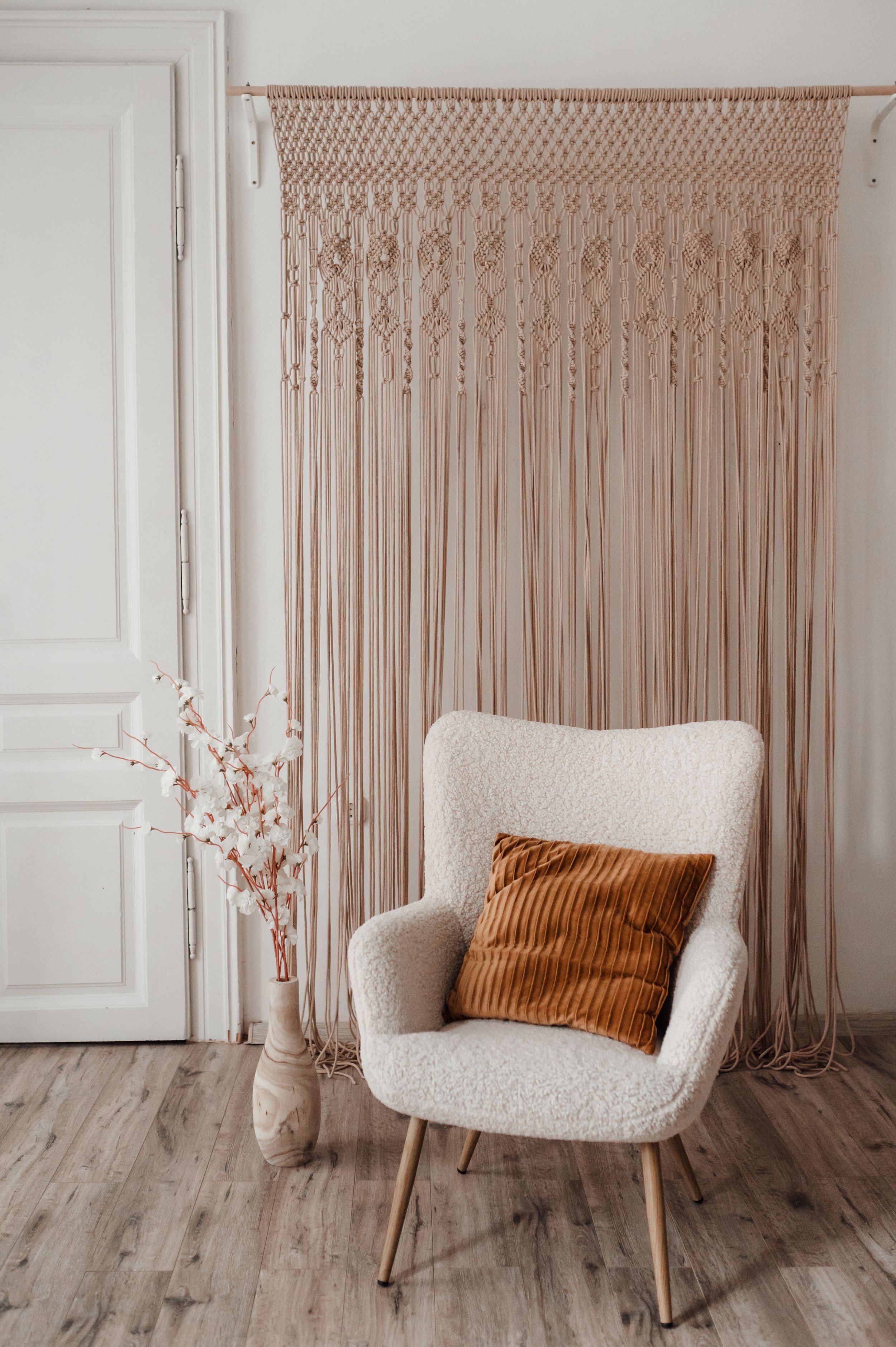 A modern boho interior with macrame wall hanging, white chair and orange accent pillow.
