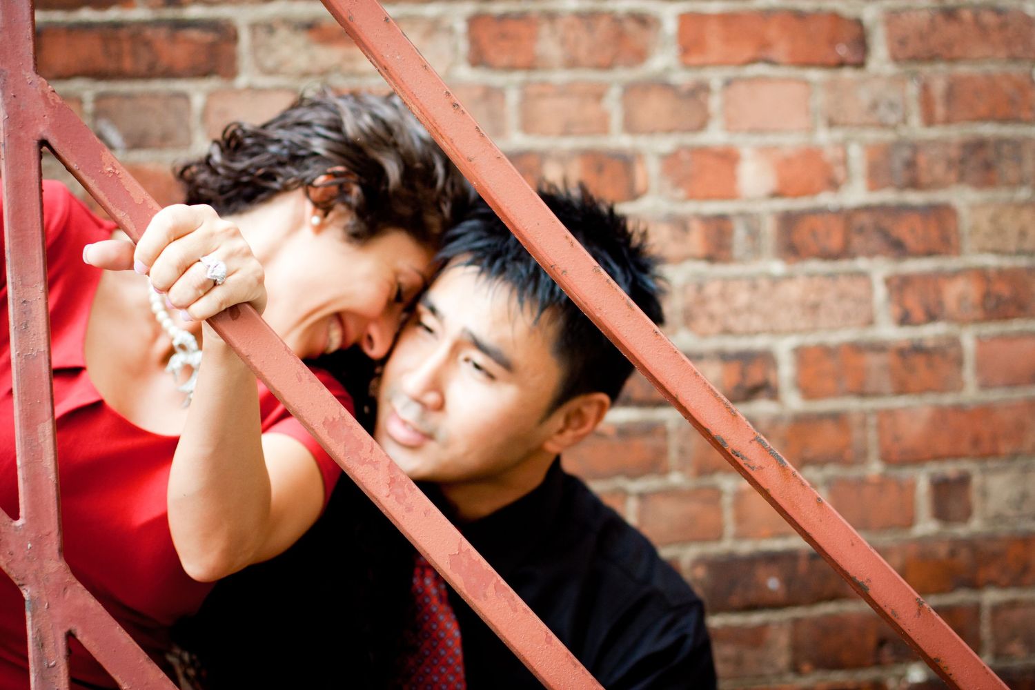 Couple sharing an intimate moment on red metal stairs against a brick wall during their engagement session.