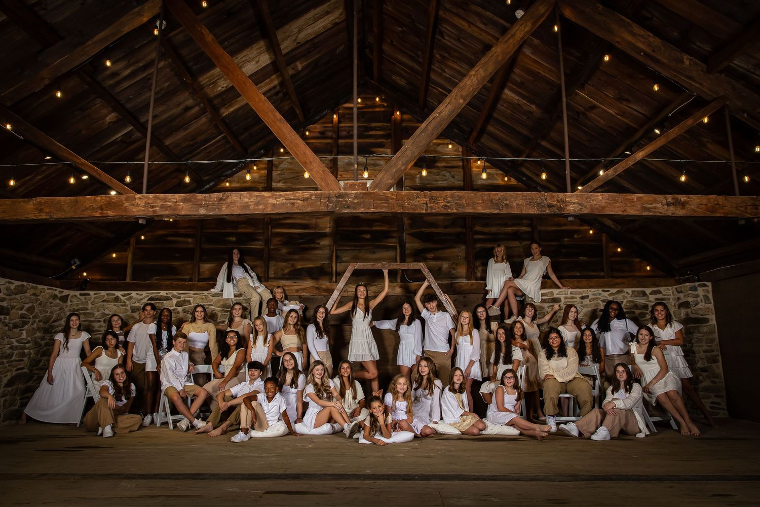 Large group celebration photo in rustic barn venue with exposed wooden beams and string lights.