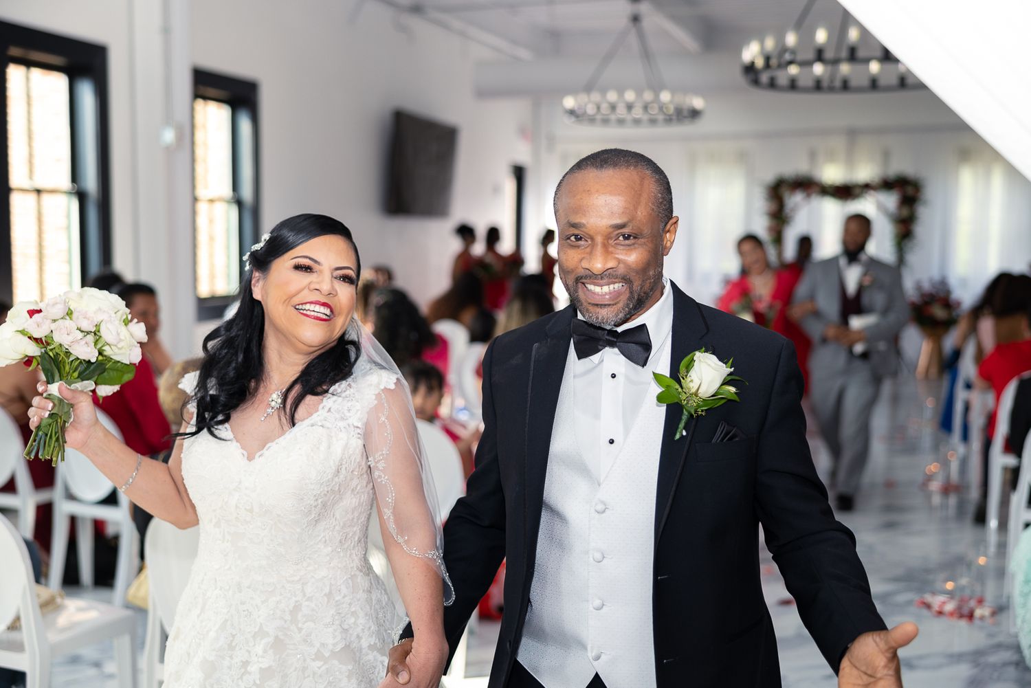 A joyful couple exits their wedding ceremony in formal attire at a bright indoor venue.