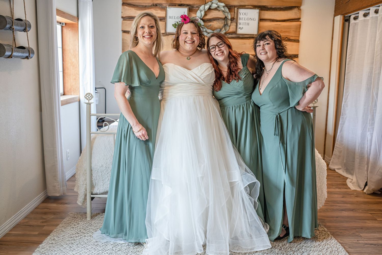 A bridal party poses together in sage green bridesmaid dresses and a white wedding gown.