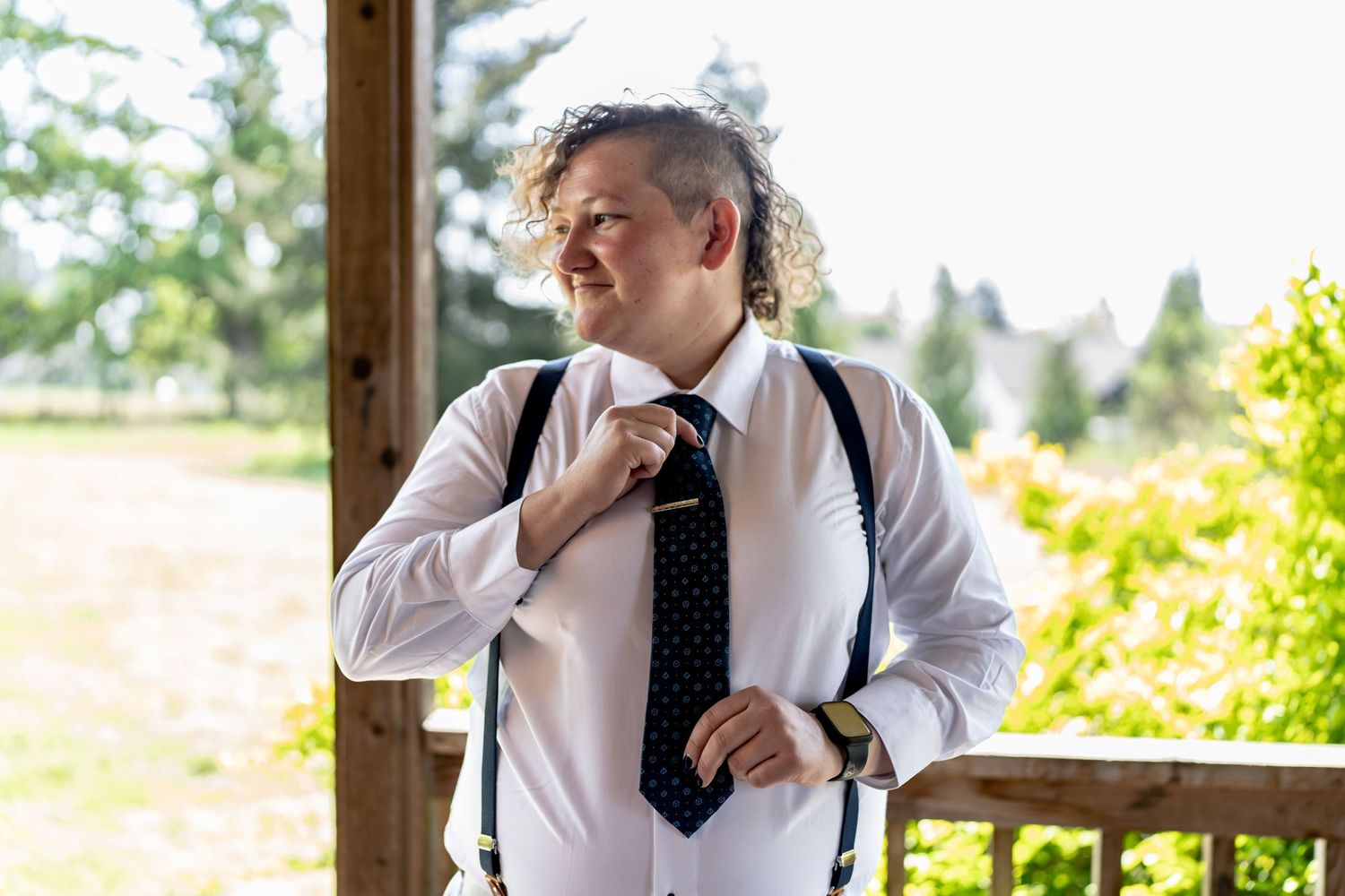 A person adjusts their tie while getting ready for a wedding on a sunny porch.