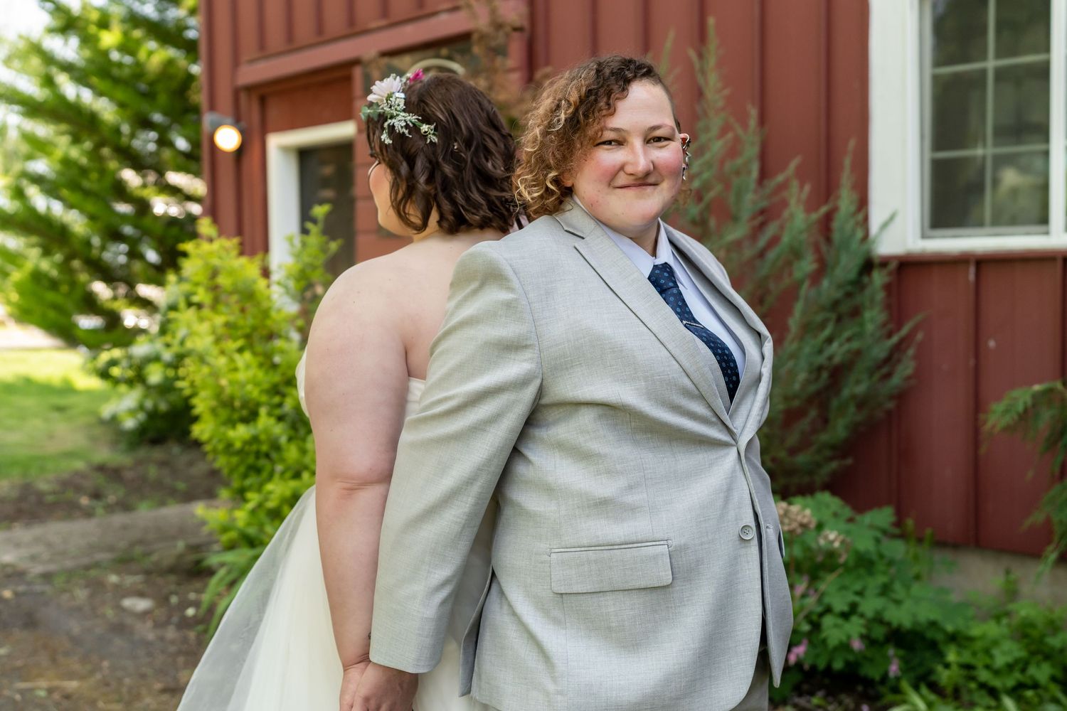 A wedding couple shares a tender moment outside a red barn building.