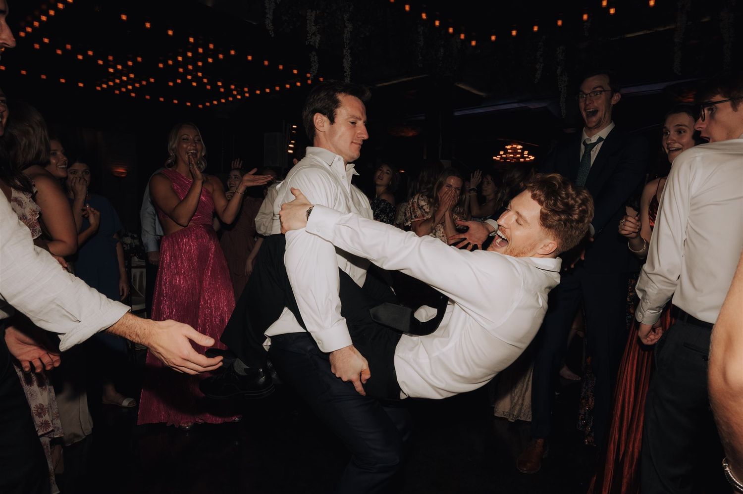 Wedding party engaging in energetic dance moves during a reception celebration.